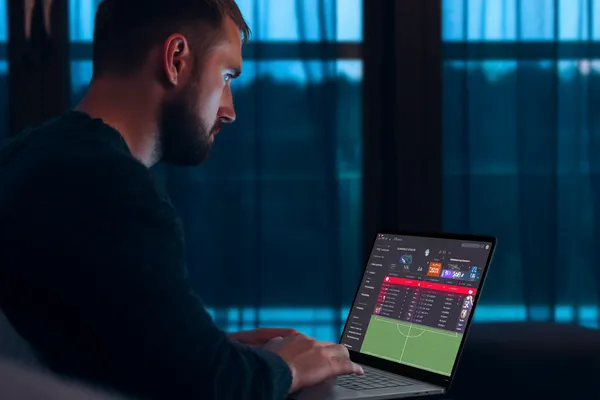 A man focused on his laptop with live stats in the background, highlighting the dedicated sports and gaming features of the UUOK mobile app.