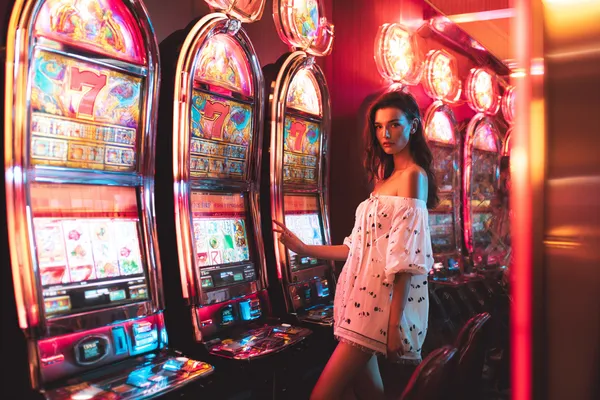 A stylish woman beside vibrant slot machines displaying glowing sevens, showcasing the variety of top slots at UUOK.